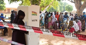 A polling station showing a voter in a booth and others in a queue